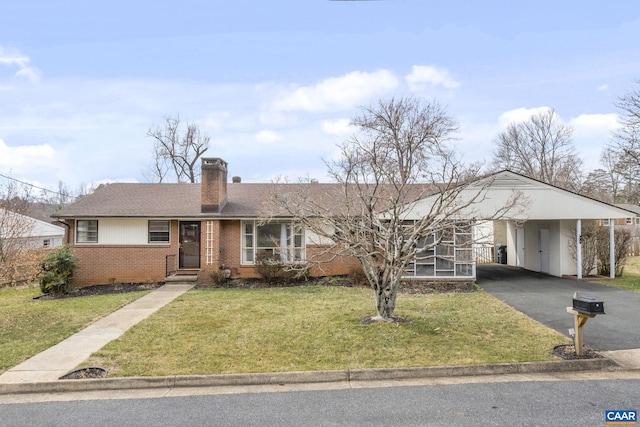 single story home featuring brick siding, an attached carport, a front yard, a chimney, and driveway