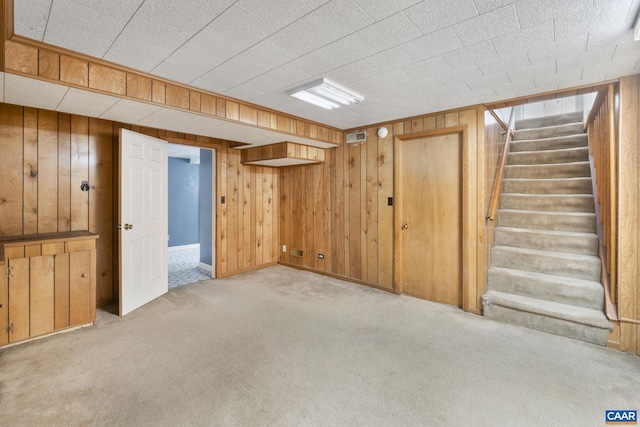 finished below grade area with visible vents, light colored carpet, wood walls, and stairs