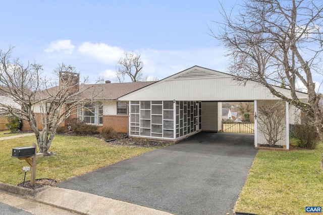 view of front facade with a chimney, a front lawn, driveway, a carport, and brick siding