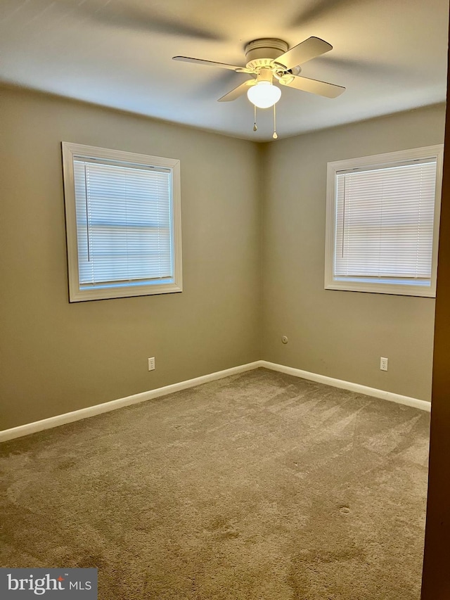 spare room with a wealth of natural light, baseboards, carpet, and a ceiling fan