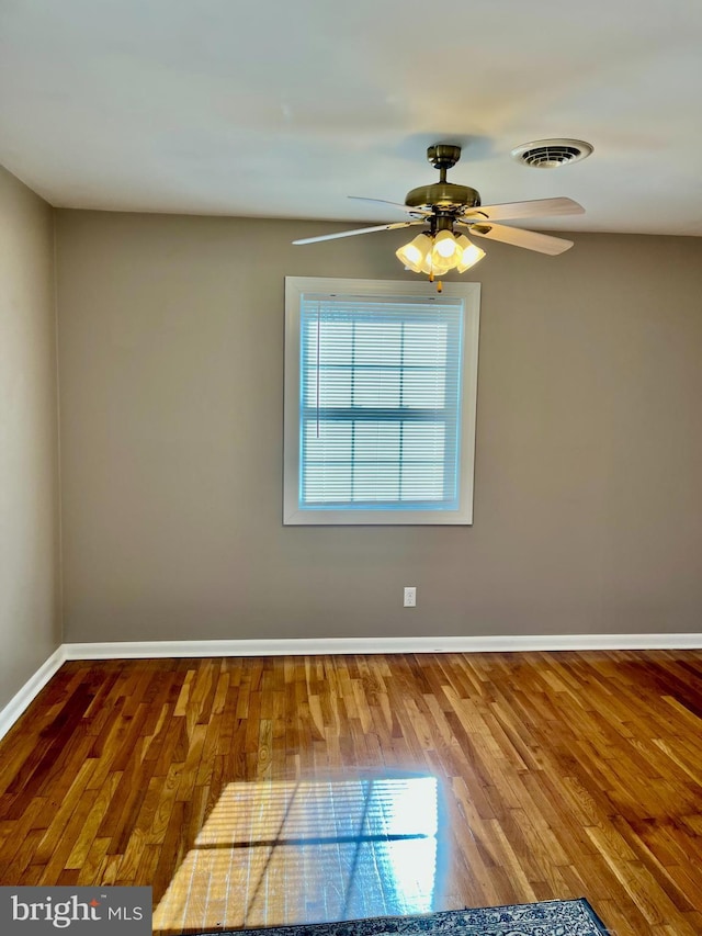 spare room featuring visible vents, a ceiling fan, baseboards, and wood finished floors