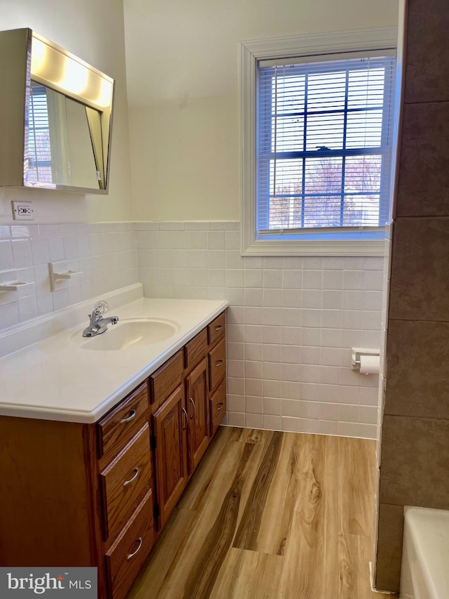 bathroom featuring a washtub, vanity, wainscoting, wood finished floors, and tile walls