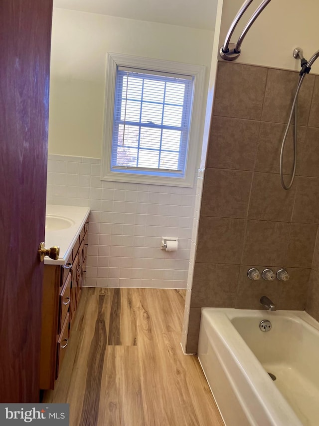 full bathroom featuring wood finished floors, tile walls, wainscoting,  shower combination, and vanity