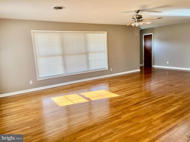 spare room featuring wood finished floors, baseboards, visible vents, and ceiling fan