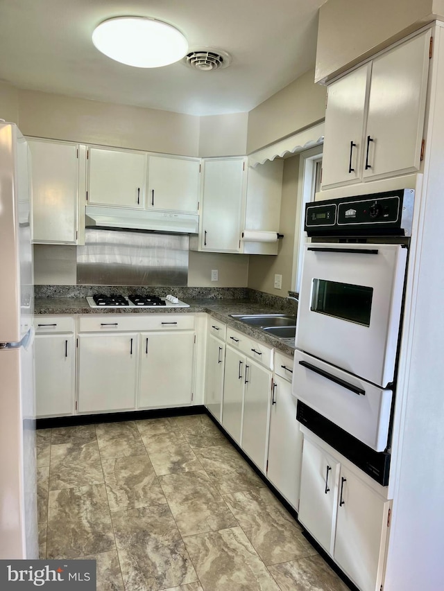 kitchen featuring white appliances, visible vents, a sink, dark countertops, and a warming drawer