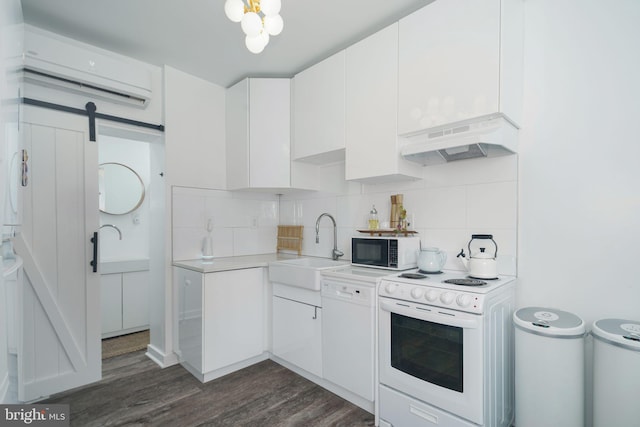 kitchen featuring under cabinet range hood, a sink, tasteful backsplash, a barn door, and white appliances