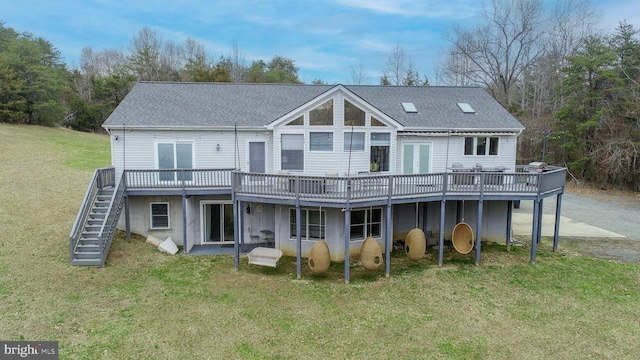 rear view of property featuring a deck, stairway, a lawn, and a shingled roof