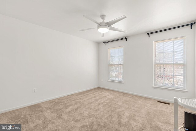 carpeted spare room with visible vents, baseboards, and a ceiling fan