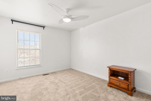 carpeted spare room with visible vents, baseboards, and ceiling fan