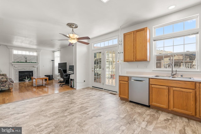 kitchen with light countertops, a fireplace, stainless steel dishwasher, brown cabinetry, and a sink