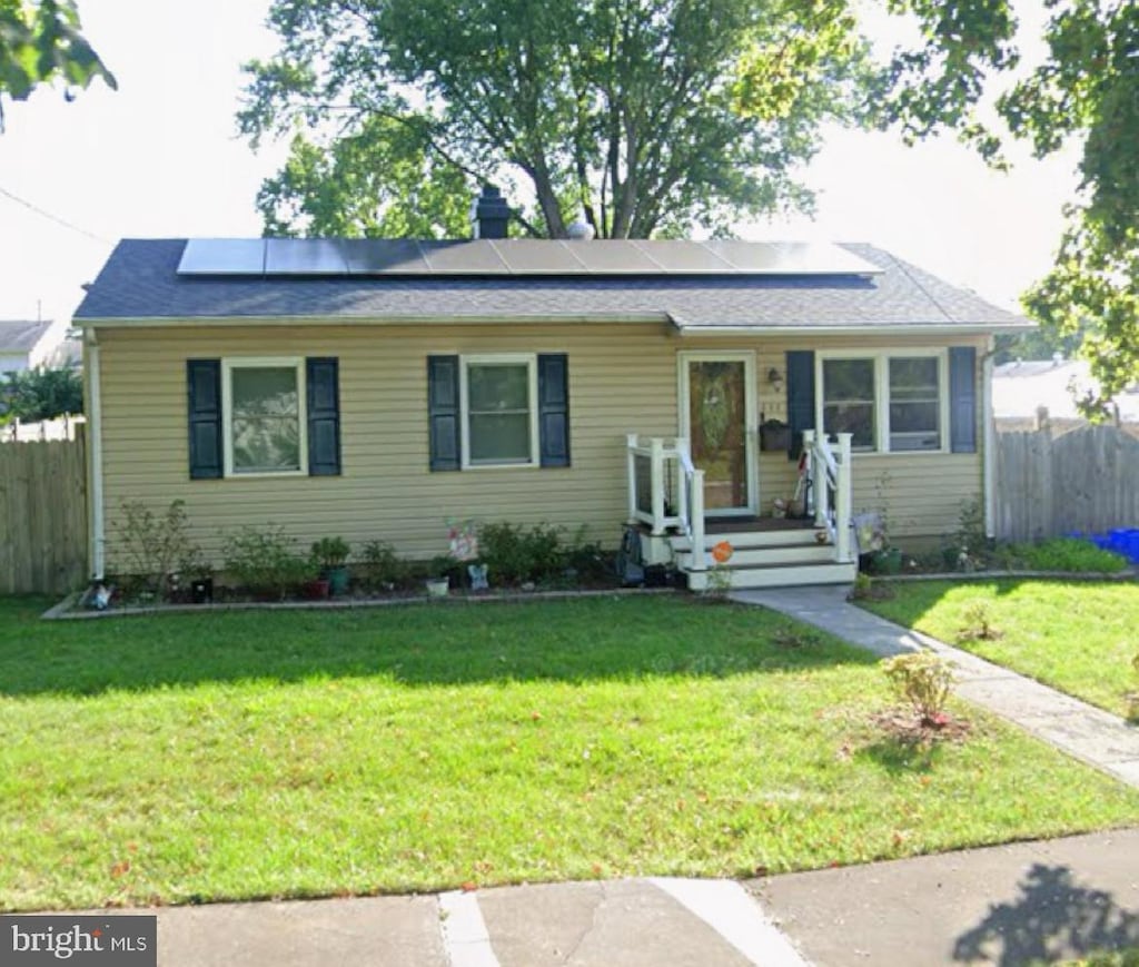 ranch-style home with solar panels, a front yard, and fence