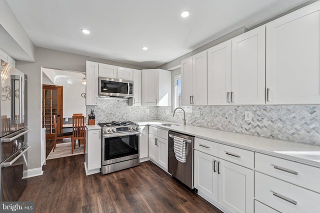 kitchen featuring a sink, tasteful backsplash, stainless steel appliances, white cabinets, and dark wood-style flooring