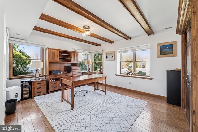 home office featuring baseboards, plenty of natural light, beam ceiling, and light wood-style flooring