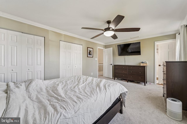 bedroom with carpet floors, two closets, ceiling fan, and crown molding