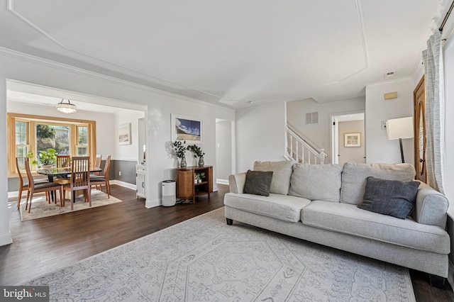 living room with stairway, baseboards, visible vents, dark wood finished floors, and ornamental molding