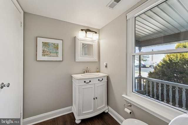 half bathroom with visible vents, baseboards, wood finished floors, and vanity