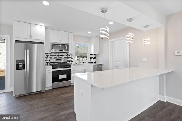 kitchen with dark wood-style floors, a peninsula, a sink, appliances with stainless steel finishes, and backsplash