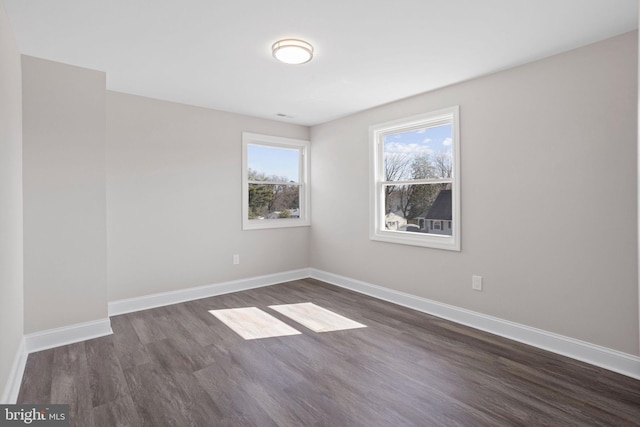 spare room with baseboards and dark wood-style floors