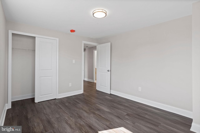 unfurnished bedroom featuring a closet, baseboards, and dark wood finished floors