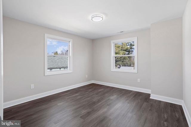 spare room featuring dark wood-type flooring, a healthy amount of sunlight, baseboards, and visible vents