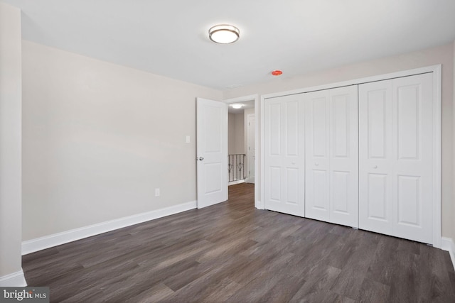 unfurnished bedroom featuring baseboards, dark wood-style flooring, and a closet