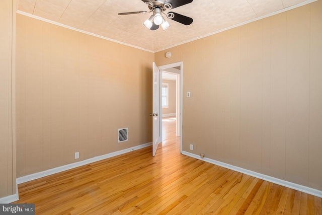 spare room featuring visible vents, ornamental molding, light wood finished floors, baseboards, and ceiling fan