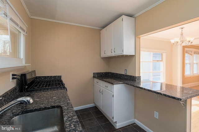 kitchen with a sink, dark stone countertops, white cabinetry, a peninsula, and crown molding