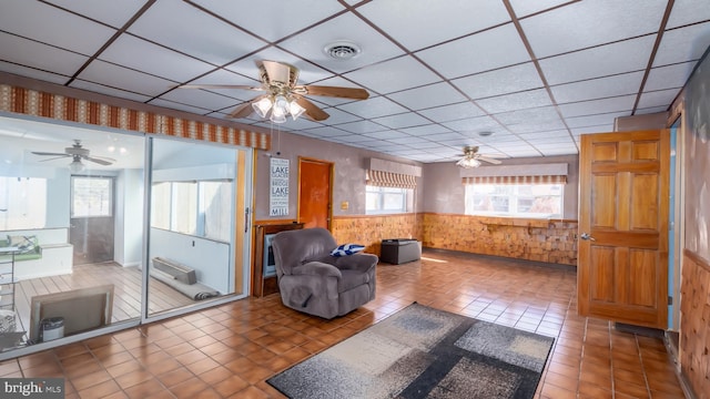 living room featuring a wainscoted wall, visible vents, a drop ceiling, tile patterned flooring, and ceiling fan