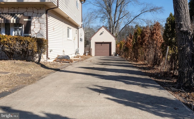 view of property exterior with a detached garage, an outdoor structure, and driveway