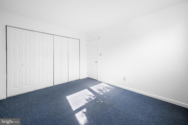 unfurnished bedroom featuring baseboards, dark colored carpet, and a closet