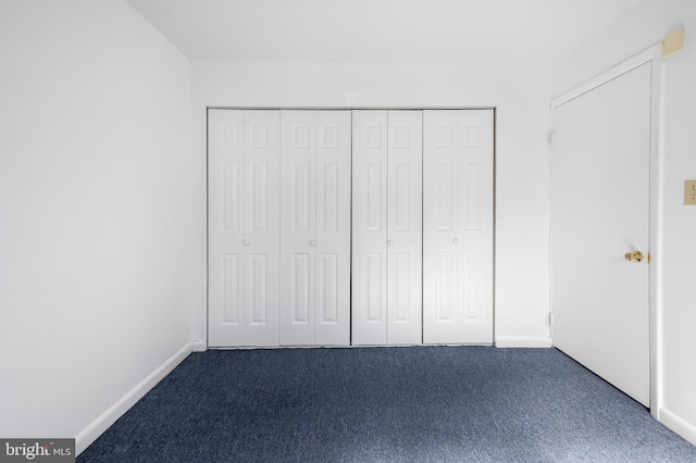 unfurnished bedroom with a closet, baseboards, and dark carpet