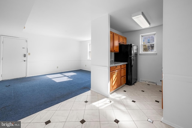 kitchen with visible vents, a healthy amount of sunlight, light carpet, freestanding refrigerator, and brown cabinetry