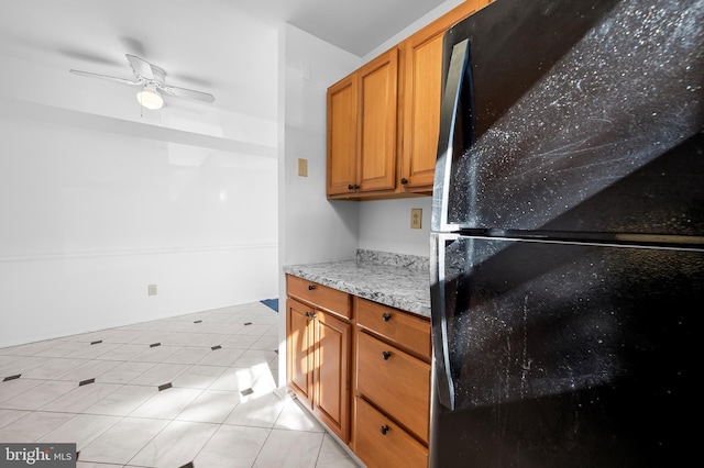 kitchen with light stone counters, a ceiling fan, light tile patterned floors, brown cabinetry, and freestanding refrigerator