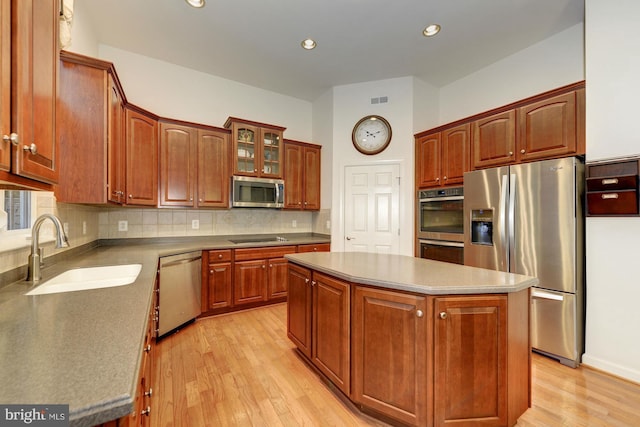 kitchen featuring light wood-type flooring, a sink, a center island, appliances with stainless steel finishes, and decorative backsplash