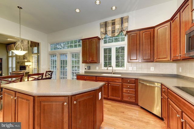 kitchen with backsplash, light wood-type flooring, a stone fireplace, appliances with stainless steel finishes, and a sink