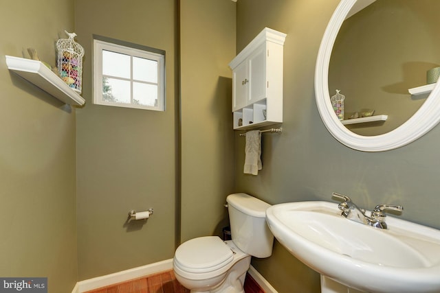 half bath with wood finished floors, toilet, baseboards, and a sink