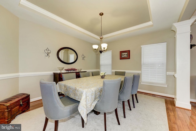 dining room with ornate columns, an inviting chandelier, light wood-style floors, and a tray ceiling