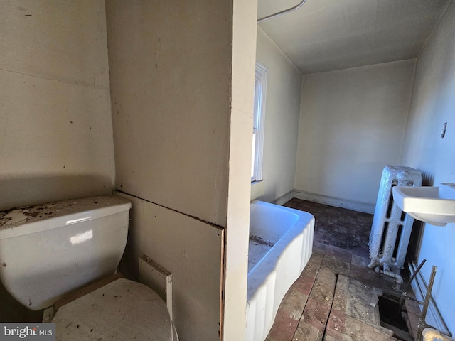 bathroom featuring a bathing tub, toilet, and stone finish flooring