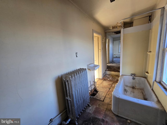 bathroom with a bath, stone tile floors, and radiator heating unit