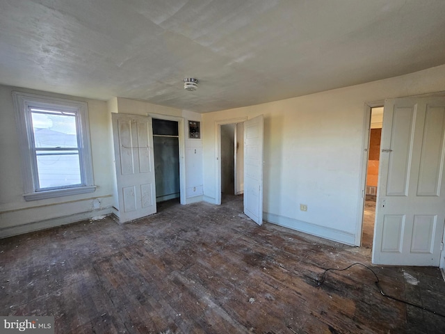 unfurnished bedroom featuring a baseboard heating unit, hardwood / wood-style flooring, baseboards, and a closet