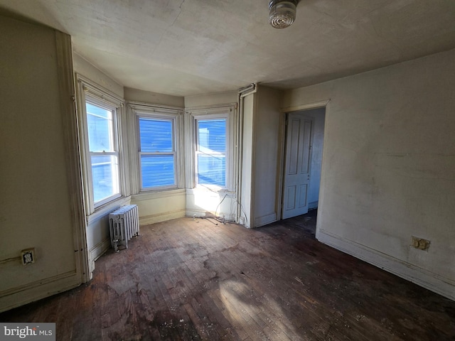 empty room featuring baseboards, a healthy amount of sunlight, radiator heating unit, and hardwood / wood-style flooring