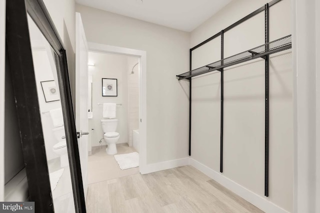 bathroom featuring wood finished floors, toilet, baseboards, and washtub / shower combination