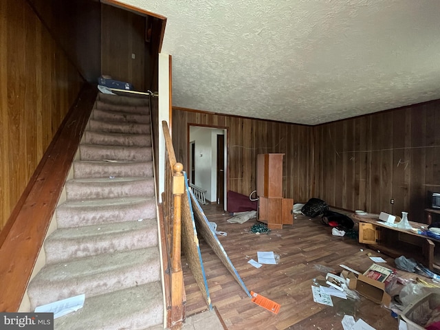 staircase featuring wooden walls, wood finished floors, and a textured ceiling