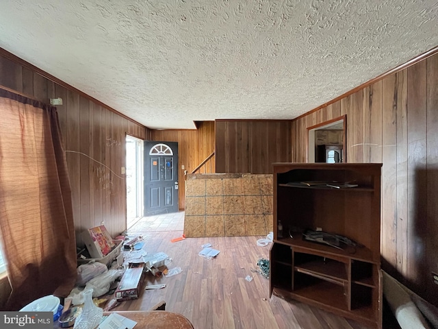 living room featuring wooden walls, a textured ceiling, crown molding, and wood finished floors