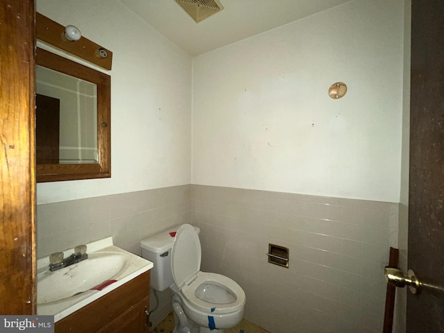 half bath featuring visible vents, a wainscoted wall, toilet, tile walls, and vanity