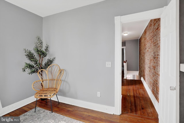 sitting room with baseboards, wood finished floors, and brick wall