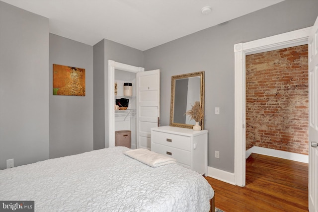 bedroom featuring wood finished floors, baseboards, and brick wall