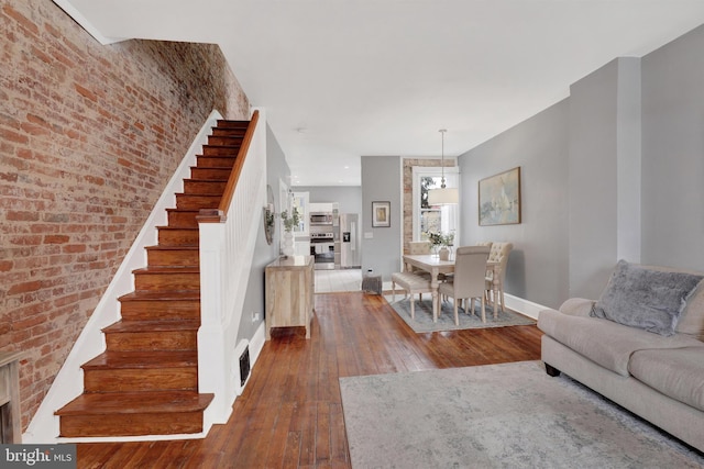 unfurnished living room featuring visible vents, brick wall, baseboards, stairway, and hardwood / wood-style floors