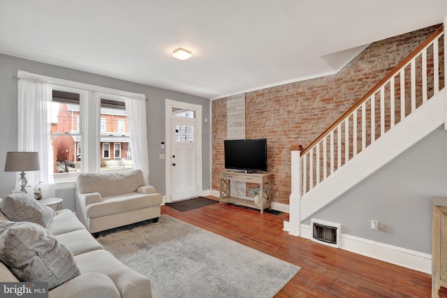 living room featuring visible vents, brick wall, baseboards, stairs, and wood finished floors