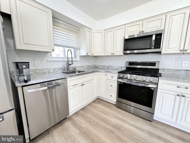 kitchen featuring backsplash, light wood-type flooring, light stone counters, appliances with stainless steel finishes, and a sink